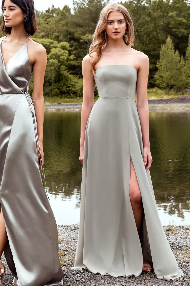 Two women in elegant bridesmaid dresses with boned bodices stand by a waterside, wearing Essie - Bridesmaid Dress by Jenny Yoo from Bergamot Bridal.