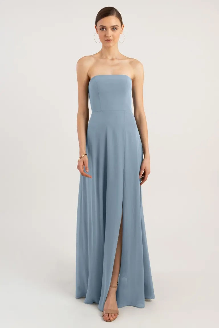 A woman posing in a strapless blue chiffon evening gown with a high slit, the Essie Bridesmaid Dress by Jenny Yoo from Bergamot Bridal.