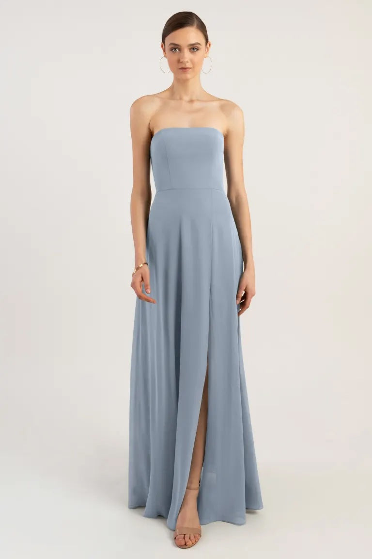 A woman in an elegant strapless neckline pale blue Essie - Bridesmaid Dress by Jenny Yoo gown with an A-line skirt and a thigh-high slit from Bergamot Bridal.