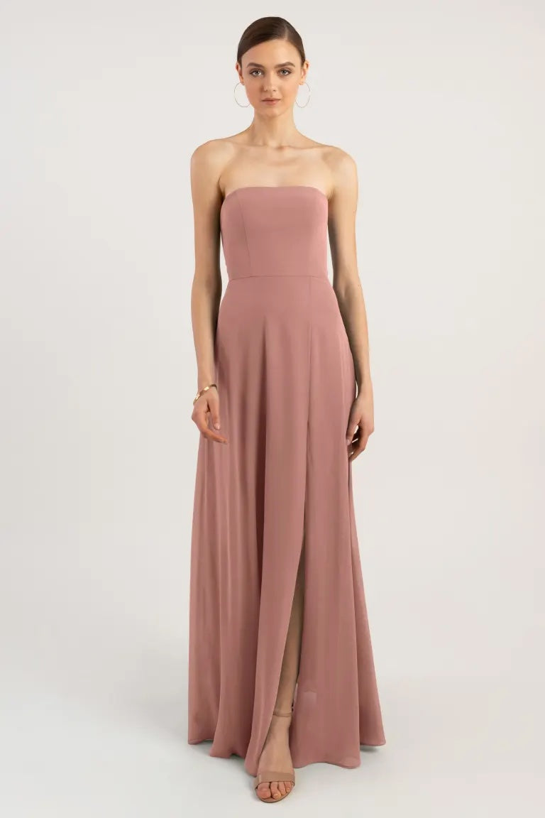Woman in a strapless blush gown with an A-line skirt standing against a white background, wearing the Essie - Bridesmaid Dress by Jenny Yoo from Bergamot Bridal.