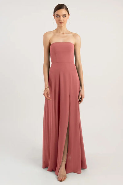 A woman standing and posing in a strapless coral chiffon evening gown with a thigh-high slit, the Essie - Bridesmaid Dress by Jenny Yoo from Bergamot Bridal.