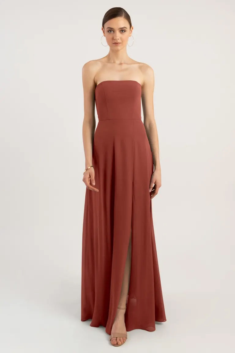Woman modeling a strapless terracotta chiffon evening gown with a thigh-high slit by Bergamot Bridal.