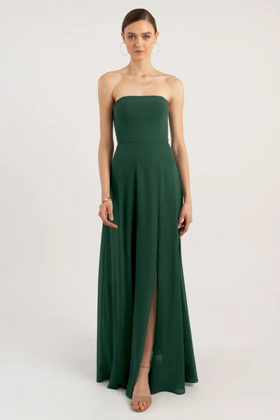 Woman standing in a strapless green evening gown with an A-line skirt and a slit, the Essie - Bridesmaid Dress by Jenny Yoo from Bergamot Bridal.