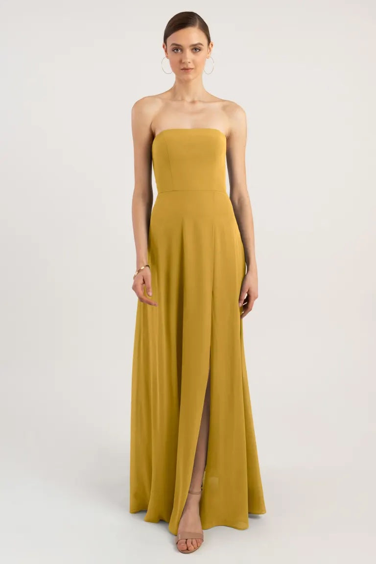 Woman in a Bergamot Bridal chiffon bridesmaid dress with a sleek straight neckline, strapless mustard evening gown with a thigh-high slit and A-line skirt.