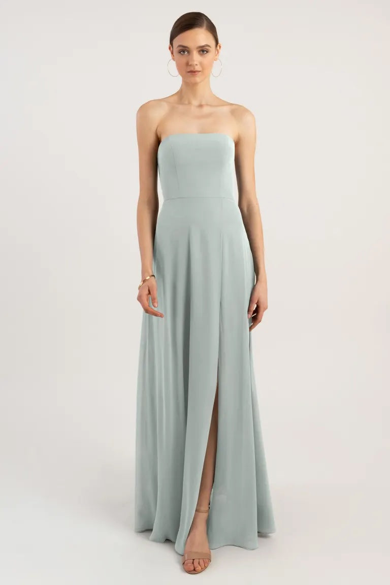 Woman posing in an elegant light blue Essie - Bridesmaid Dress by Jenny Yoo with a strapless neckline and a slit from Bergamot Bridal.