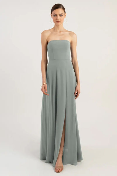 Woman posing in an elegant strapless Essie - Bridesmaid Dress by Jenny Yoo chiffon bridesmaid dress with a sleek straight neckline and a high slit from Bergamot Bridal.