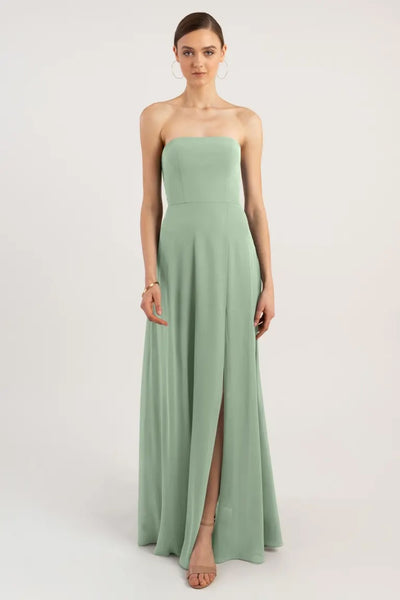 Woman standing in a pastel green strapless Essie - Bridesmaid Dress by Jenny Yoo with a thigh-high slit and a sleek A-line skirt from Bergamot Bridal.