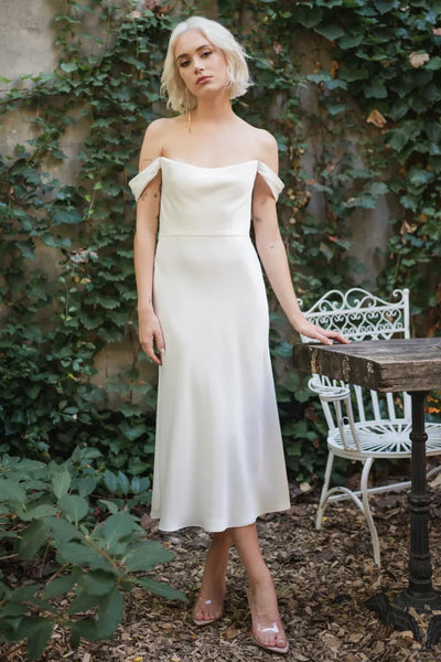A woman in the Evelyn - Jenny Yoo Little White Dress, potentially a wedding dress, is posing in front of a table from Bergamot Bridal.