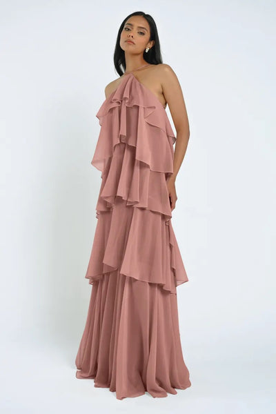 Woman in a layered, ruffled, blush-colored Farley Bridesmaid Dress by Jenny Yoo from Bergamot Bridal standing against a plain background.