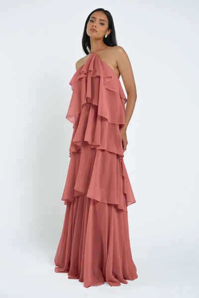 Person wearing the Farley Bridesmaid Dress by Jenny Yoo from Bergamot Bridal, a sleeveless, tiered gown in dusty rose chiffon with layered ruffles. They are standing against a plain white background. The dress exudes an effortless feel, perfectly capturing elegance and grace.