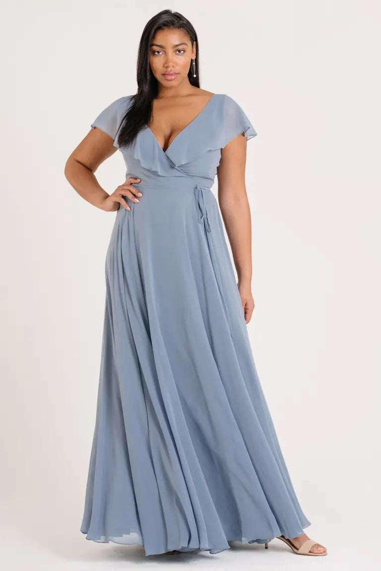 Woman in a blue chiffon Faye - Bridesmaid Dress by Jenny Yoo with a v-neckline and flutter sleeve posing for the camera.