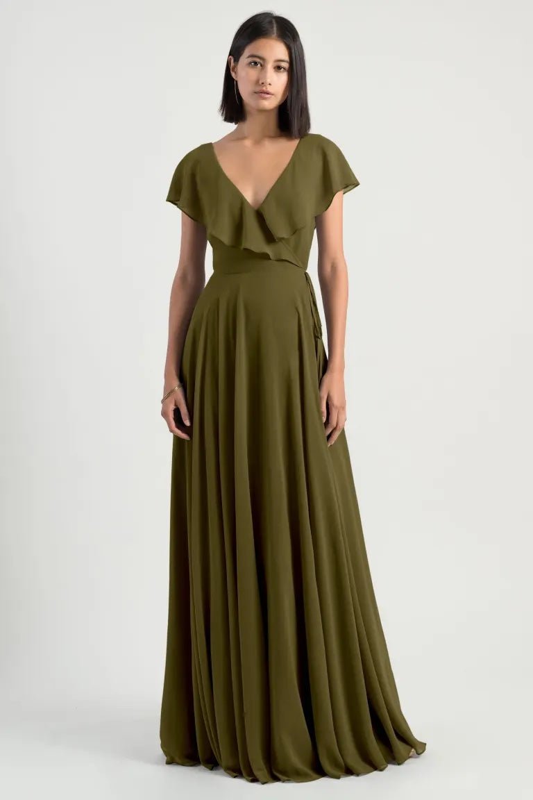 A woman in a full-length olive green chiffon wrap dress with a v-neckline and flutter sleeves by Bergamot Bridal's Faye - Bridesmaid Dress by Jenny Yoo.