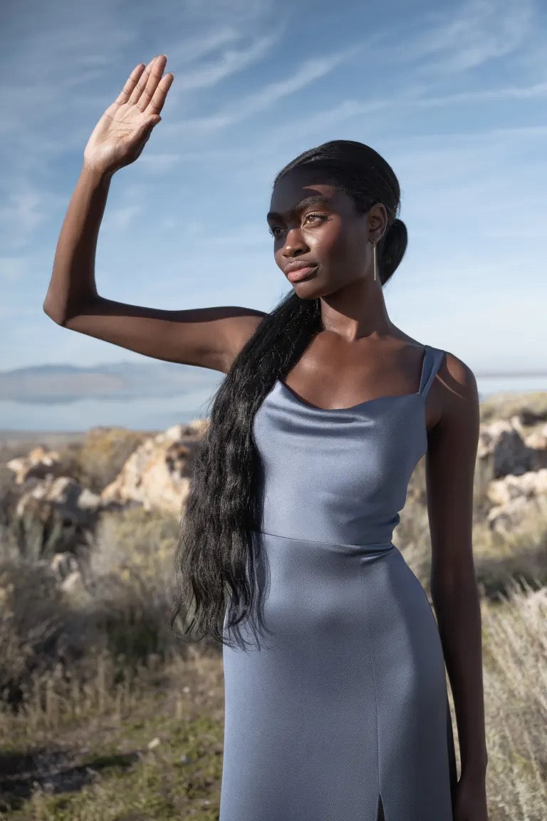 Woman shielding her eyes from the sun while standing outdoors, in a Gina bridesmaid dress by Jenny Yoo with an A-line skirt from Bergamot Bridal.