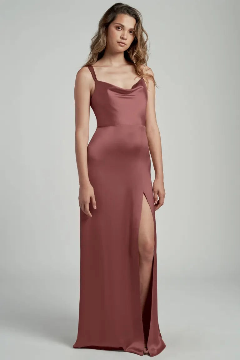 Woman posing in a sleek, dusty rose satin bridesmaid dress with a thigh-high slit and cowl neckline called Gina by Jenny Yoo from Bergamot Bridal.