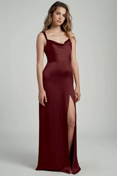 A woman in an elegant maroon satin bridesmaid dress with a cowl neckline and thigh-high slit, the Gina Bridesmaid Dress by Jenny Yoo from Bergamot Bridal.