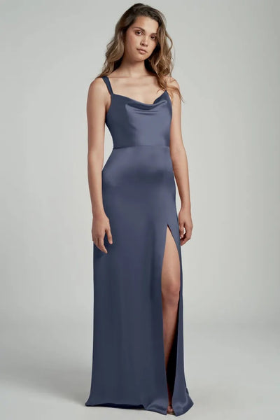 Woman posing in a sleek blue satin bridesmaid dress with a cowl neckline and a thigh-high slit, the Gina Bridesmaid Dress by Jenny Yoo from Bergamot Bridal.