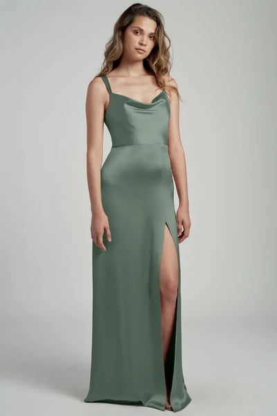 Woman in an elegant green satin Gina - Bridesmaid Dress by Jenny Yoo from Bergamot Bridal with a side slit posing against a neutral background.