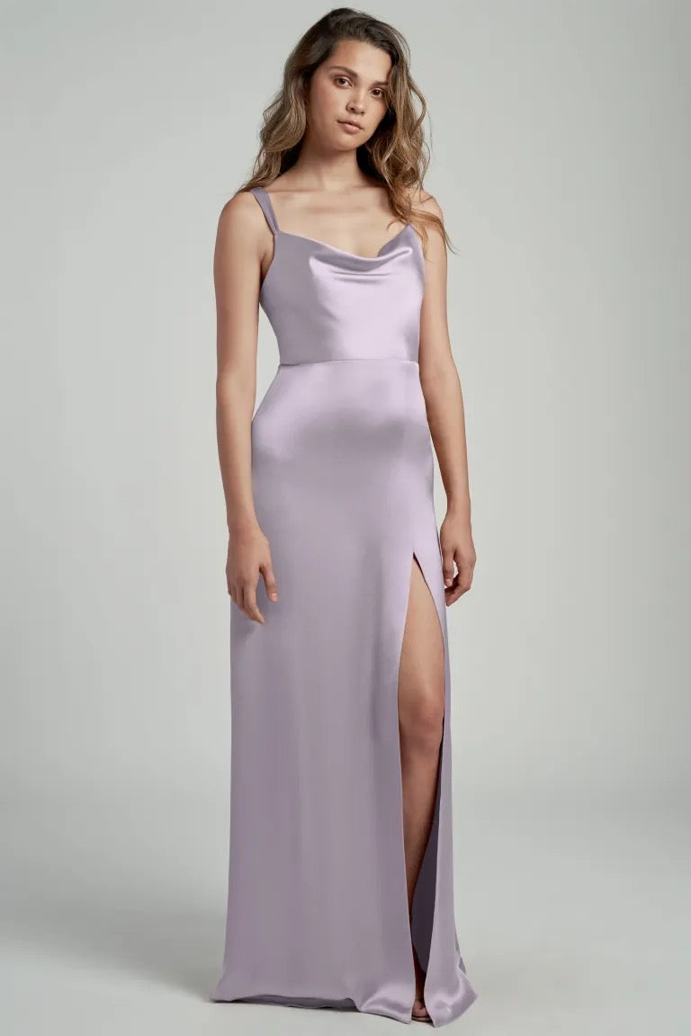 A woman wearing a long lilac satin bridesmaid dress with a thigh-high slit and a cowl neckline by Gina - Bridesmaid Dress from Jenny Yoo at Bergamot Bridal.