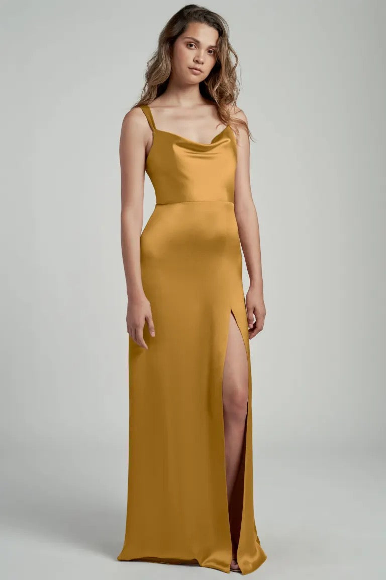 Woman posing in a sleek gold satin bridesmaid dress with a thigh-high slit and cowl neckline, the Gina Bridesmaid Dress by Jenny Yoo from Bergamot Bridal.