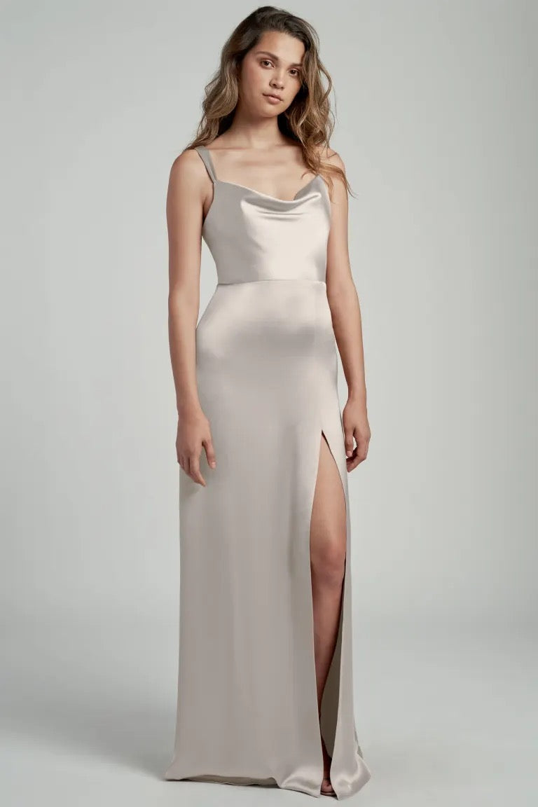 A woman wearing an elegant, cowl neckline, sleeveless Gina - Bridesmaid Dress by Jenny Yoo with a thigh-high slit and an A-line skirt from Bergamot Bridal.