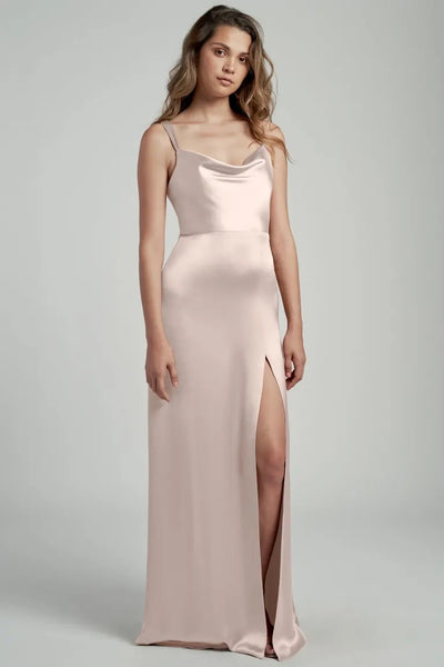 Woman posing in an elegant pale pink satin Gina bridesmaid dress by Jenny Yoo with a cowl neckline and thigh-high slit from Bergamot Bridal.