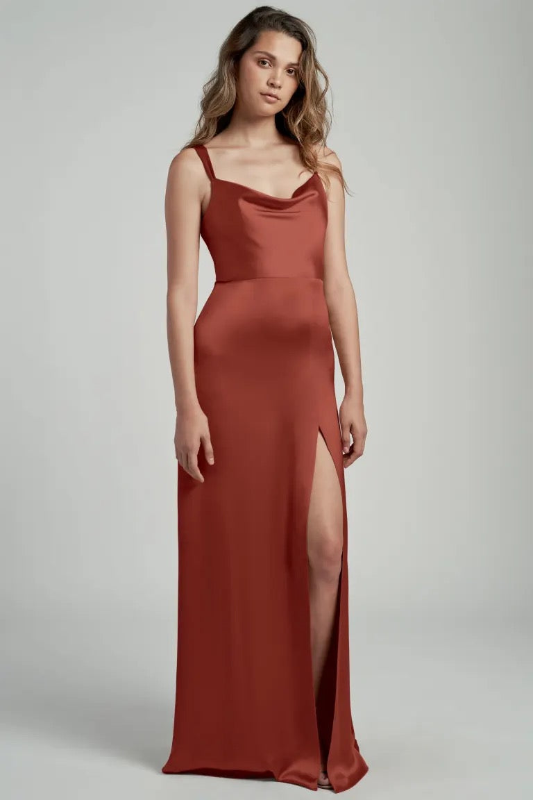 A woman in a long, elegant rust-colored satin bridesmaid dress with a cowl neckline and an A-line skirt, the Gina Bridesmaid Dress by Jenny Yoo at Bergamot Bridal.