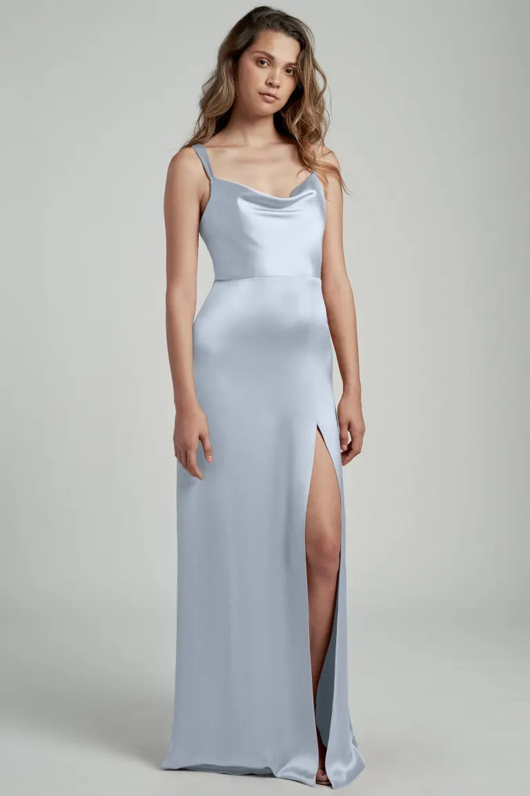 A woman in a light blue satin bridesmaid dress with a cowl neckline and a thigh-high slit, the Gina Bridesmaid Dress by Jenny Yoo from Bergamot Bridal.