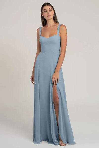 Woman in an elegant blue chiffon bridesmaid dress with a high slit and sweetheart neckline posing against a neutral background, wearing the Harris bridesmaid dress by Jenny Yoo from Bergamot Bridal.