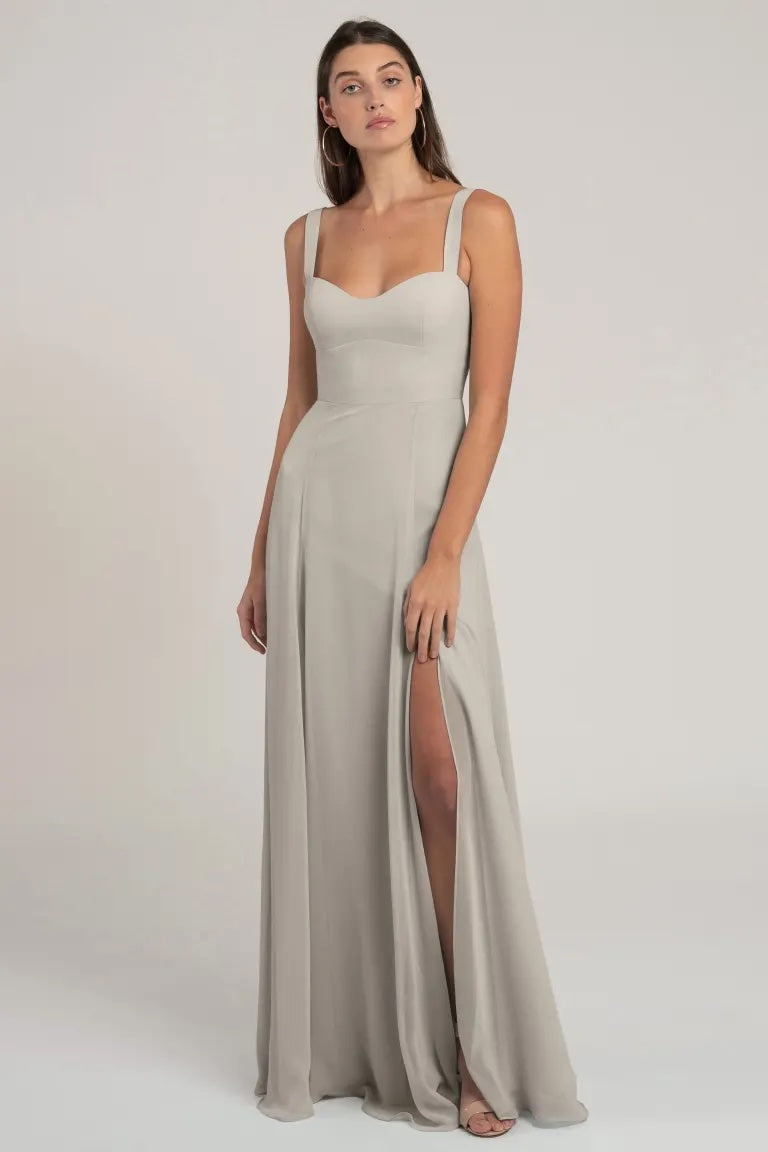 Woman standing in a beige chiffon bridesmaid dress with a bombshell neckline and a thigh-high slit, the Harris by Jenny Yoo from Bergamot Bridal.