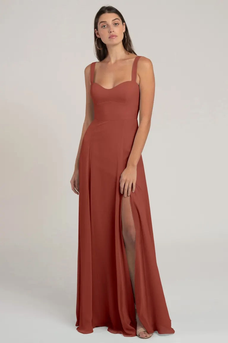 Woman in an elegant burnt orange evening gown with a flattering silhouette and a side slit - Harris Bridesmaid Dress by Jenny Yoo from Bergamot Bridal.