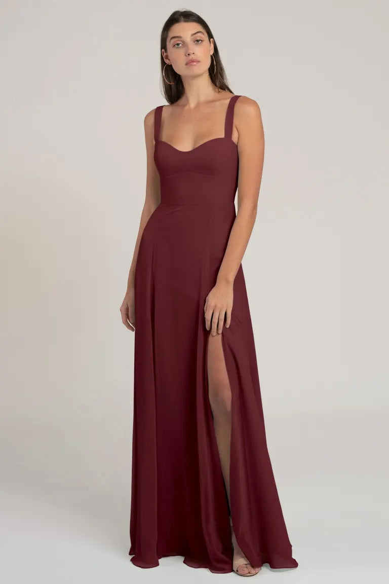 Woman in an elegant burgundy chiffon evening gown with a flattering silhouette and a thigh-high slit, the Harris bridesmaid dress by Jenny Yoo from Bergamot Bridal.