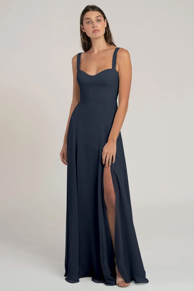 A woman modeling a flattering silhouette chiffon navy blue evening gown with a slit, the Harris Bridesmaid Dress by Jenny Yoo from Bergamot Bridal.