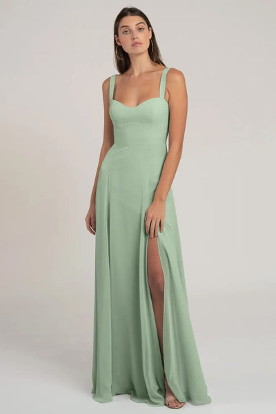 Woman in an elegant mint green chiffon Harris bridesmaid dress by Jenny Yoo with a bombshell neckline and a slit from Bergamot Bridal.
