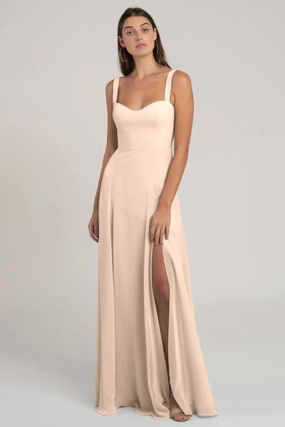 Woman posing in an elegant beige chiffon bridesmaid dress with a thigh-high slit and a sweetheart neckline, the Harris Bridesmaid Dress by Jenny Yoo from Bergamot Bridal.