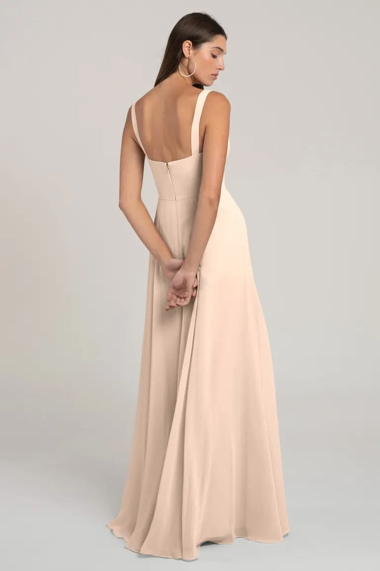 Woman wearing a Harris Bridesmaid Dress by Jenny Yoo in beige chiffon from Bergamot Bridal viewed from the back, showcasing a flattering silhouette.