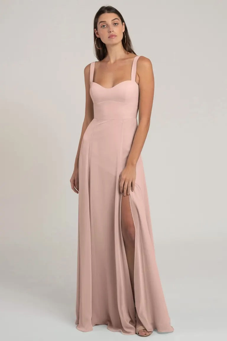 A woman posing in an elegant light pink chiffon evening gown with a thigh-high slit, Harris - Bridesmaid Dress by Jenny Yoo from Bergamot Bridal.