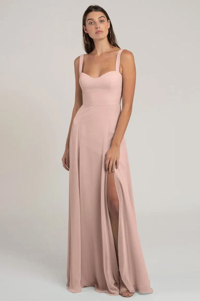 A woman posing in an elegant light pink chiffon evening gown with a thigh-high slit, Harris - Bridesmaid Dress by Jenny Yoo from Bergamot Bridal.