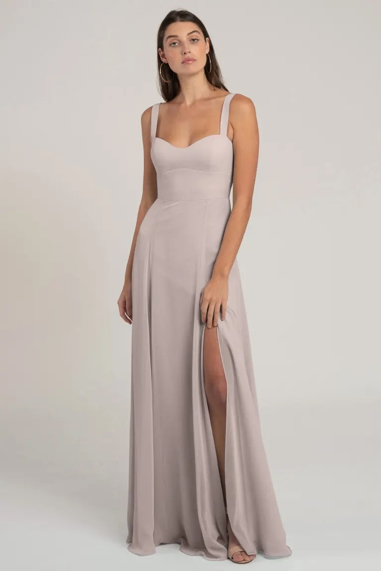 A woman in a sleeveless, light-colored Harris - Bridesmaid Dress by Jenny Yoo with a flattering silhouette and thigh-high slit posing against a neutral background.