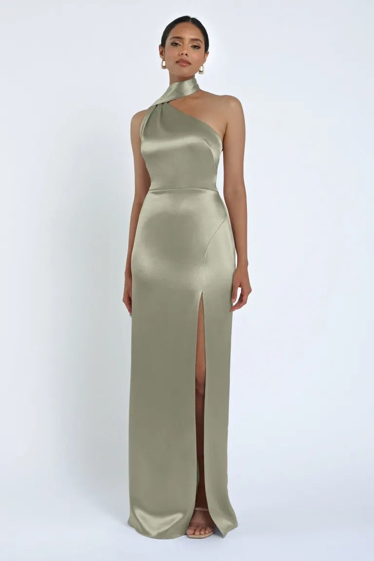 A woman in the Hepburn Bridesmaid Dress by Jenny Yoo from Bergamot Bridal, a sleeveless olive green satin gown with a high neckline and a thigh-high slit, stands against a plain white background, exuding Hollywood glam.