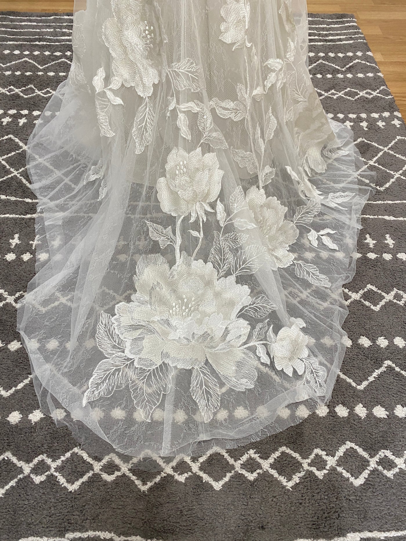 A white Willowby by Watter Honor 52122 bridal veil with floral motifs laid on a gray and white patterned Bergamot Bridal rug.