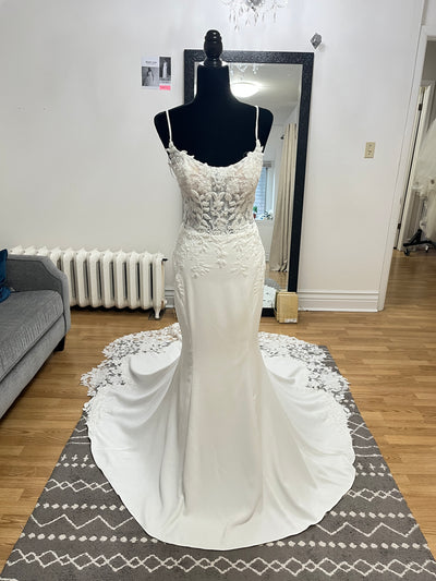 The Bergamot Bridal Crepe and Lace Fit & Flare Gown features a beaded lace bodice, beaded spaghetti straps, and a scalloped lace train, shown sleeveless on a black mannequin in a well-lit room with wooden floors.