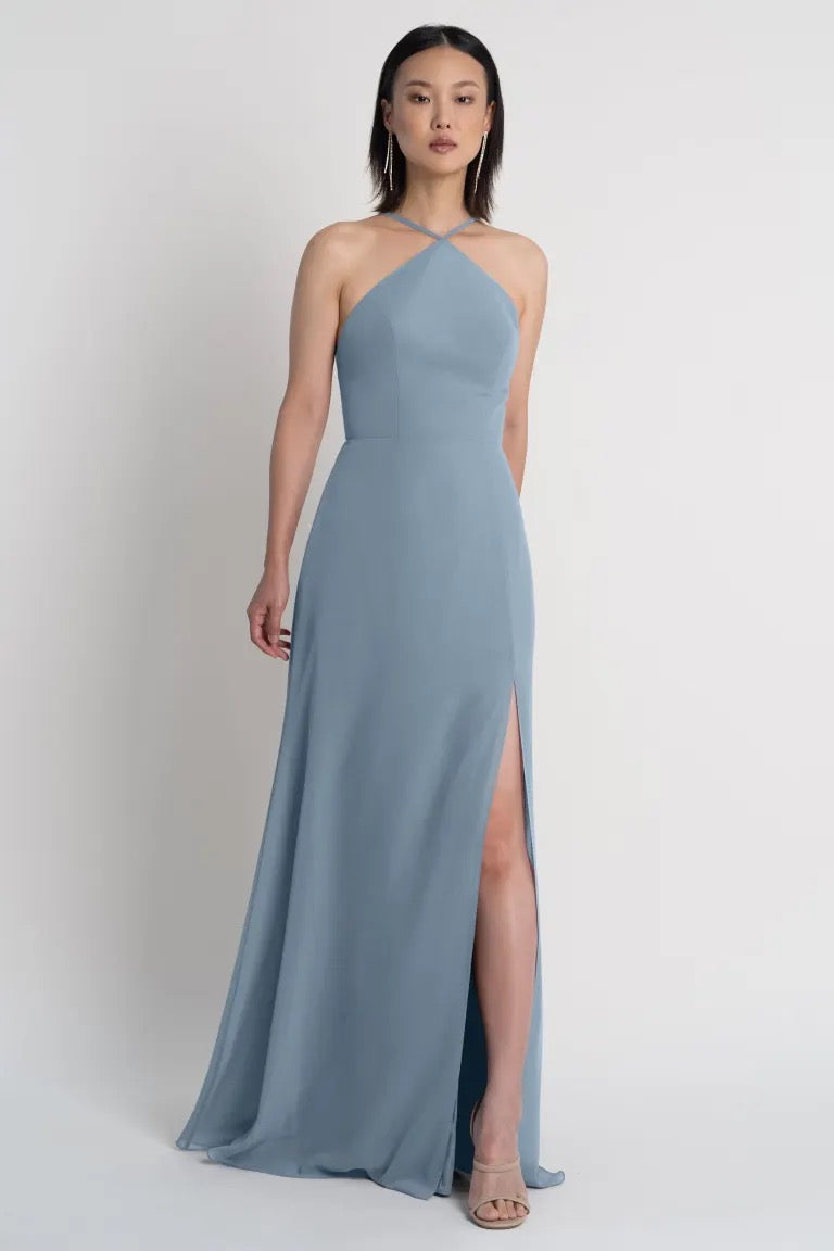A woman modeling a powder blue Ingrid bridesmaid dress by Jenny Yoo with a halter neckline and thigh-high side slit from Bergamot Bridal.