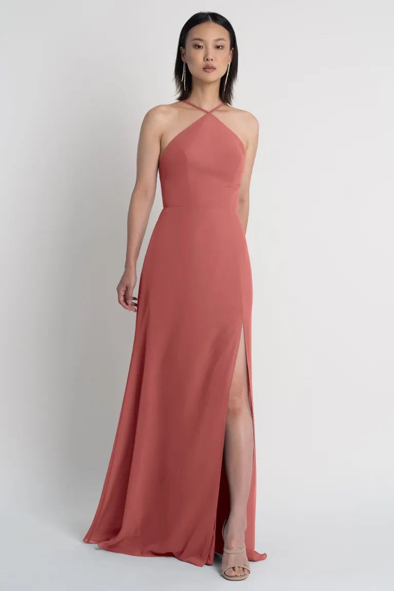 Woman in an elegant terracotta Ingrid bridesmaid dress by Jenny Yoo with a halter neckline and side slit from Bergamot Bridal.