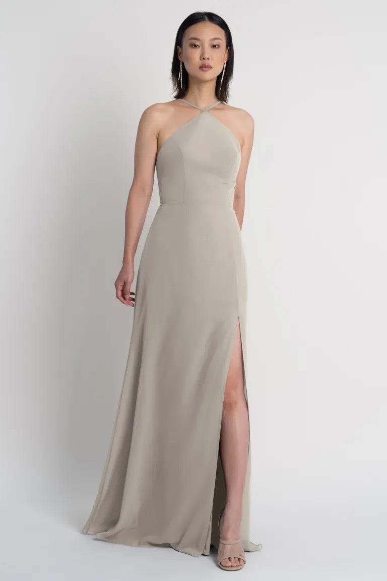 A woman modeling a Jenny Yoo bridesmaid dress featuring a beige one-shoulder evening gown with a side slit by Bergamot Bridal.