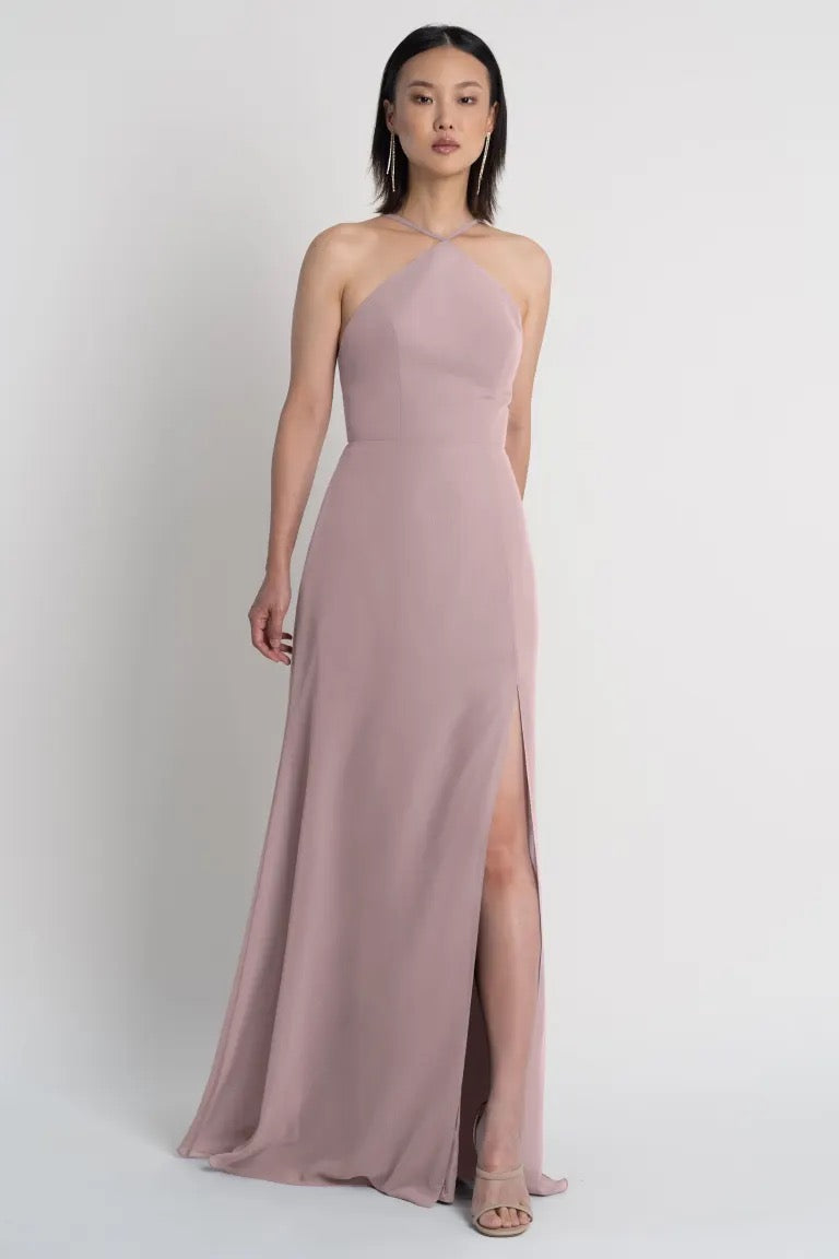 Woman in an elegant blush pink Ingrid bridesmaid dress by Jenny Yoo with a pointed halter neckline and a side slit from Bergamot Bridal.
