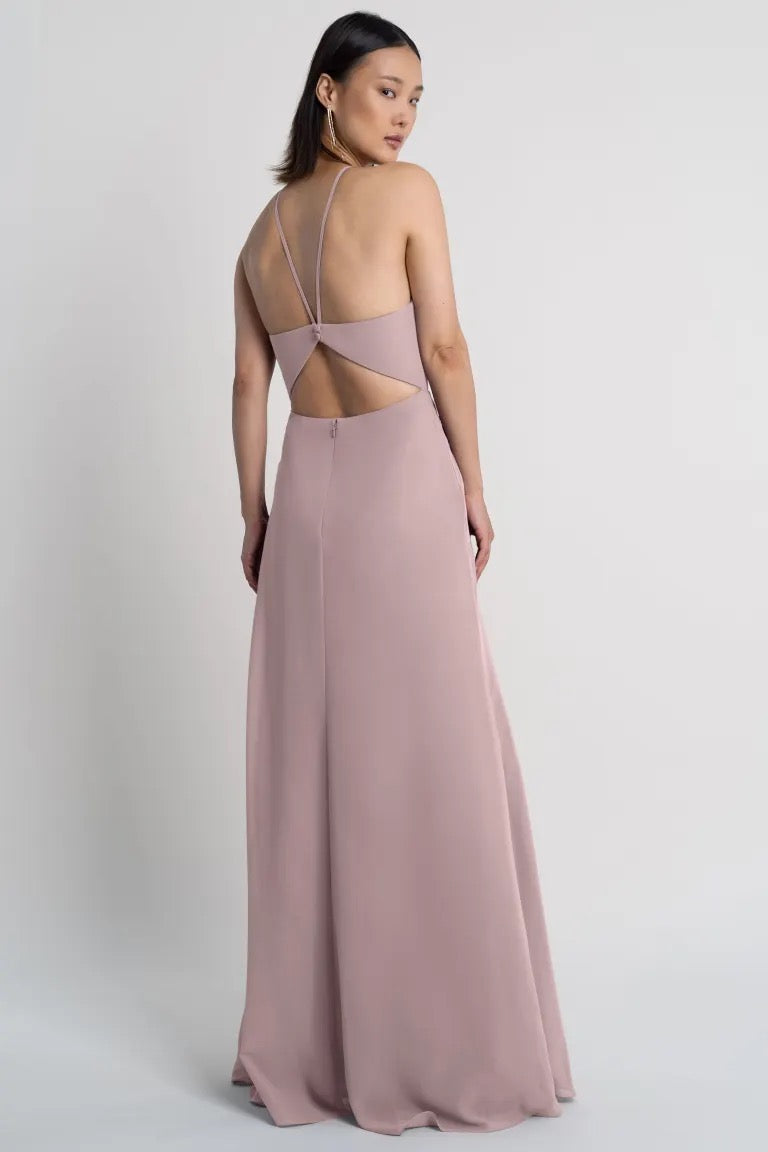 A woman models a Ingrid - Bridesmaid Dress by Jenny Yoo from Bergamot Bridal with a backless halter neckline evening gown with crisscross straps.