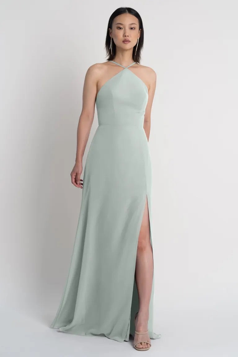 Woman posing in a light green Ingrid bridesmaid dress by Jenny Yoo with a side slit from Bergamot Bridal.