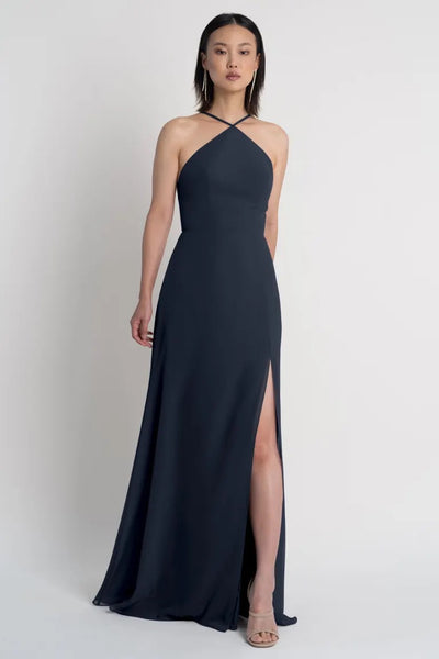 A woman in an elegant navy blue Ingrid bridesmaid dress by Jenny Yoo with a side slit from Bergamot Bridal.