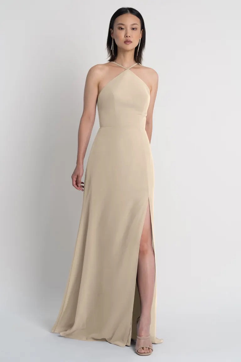 Woman in a Jenny Yoo Ingrid bridesmaid dress by Bergamot Bridal with a beige halter neckline and a side slit.