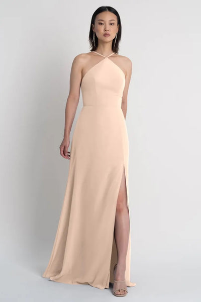 A woman in an elegant Ingrid - Bridesmaid Dress by Jenny Yoo with a thigh-high side slit standing against a neutral background.
